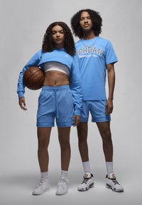 To personer i matchende lyseblå træningstøj. Den ene har en cropped sweatshirt og shorts på, mens den anden har en t-shirt og shorts.