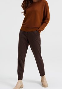 Rostfärgad ribbad tröja i kombination med bruna snäva byxor, som har en mjuk textur, samt beige ankelstövlar med en kraftig sula.