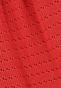 Tissu en tricot d'une couleur rouge vive présentant un motif texturé avec de petits trous ouverts disposés dans un design répétitif.