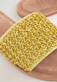 Kollane liug sandaal, millel on tekstureeritud ülemine osa lillepärlitega kaunistatud, pehme pruun suedesiseosa ja lame tall, mis tagab mugavuse.