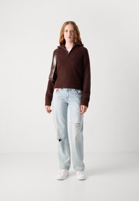 Bruine geribbelde gebreide trui met een ritskraag, gecombineerd met lichtblauwe distressed jeans en witte sneakers, met een bruine schoudertas.