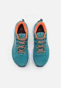 Baskets de course turquoise avec une tige en mesh texturé, des accents orange et des détails réfléchissants. Semelle blanche avec un motif de traction.