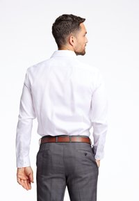 Witte blouse met lange mouwen en een puntige kraag, gecombineerd met grijs geruite broek en een bruine leren riem. Achteraanzicht getoond.