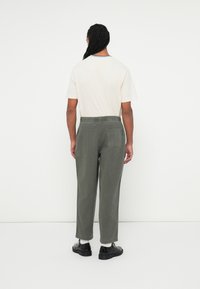 Grønne bomulds twill bukser med afslappet pasform, elastisk talje og sidelomme. Båret med en lysfarvet t-shirt og sorte sko.