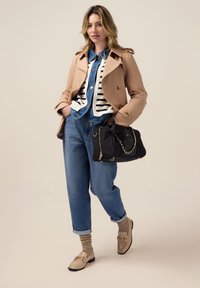 Abrigo trench beige sobre un suéter rayado, combinado con unos vaqueros de cintura alta azules. Los accesorios incluyen un bolso negro con cadena dorada y unos mocasines beige.