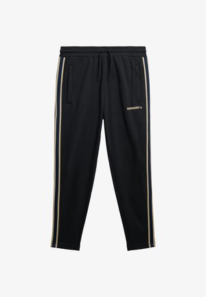 Pantaloni sportivi neri con strisce laterali beige e blu navy, vita elasticizzata con coulisse, tasche e piccolo logo "Superdry" sulla coscia.