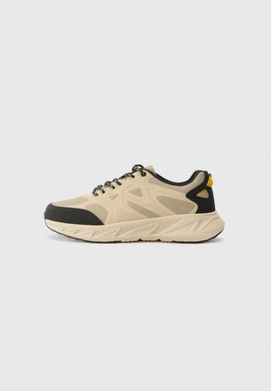 Beiger und schwarzer Sportschuh mit Mesh-Einsätzen, dicker Sohle, schwarzen Schnürsenkeln und gelbem Zuglasche an der Ferse, Seitenansicht.
