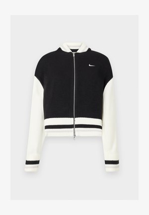 Chaqueta recortada en blanco y negro con cremallera y ribete acanalado. Presenta una textura de punto y un pequeño logo en el lado izquierdo del pecho. Acentos a rayas en las mangas.