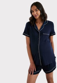 Granatowy zestaw do spania wykonany z miękkiego materiału, składający się z koszulki z krótkim rękawem zapinanej na guziki z kieszonką oraz dopasowanych szortów, oba z białymi akcentami.