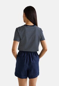 Haut à manches courtes rayé bleu marine et blanc associé à un short en lin bleu marine avec taille élastique et poches avant, vu de dos.