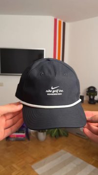 Svart caps laget av stoff med en buet skjerm, med hvit brodert tekst "nike golf inc. ETABLER 1984" og en hvit aksentbånd.