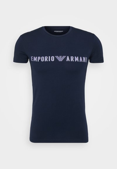 T-shirt de algodão azul marinho com decote redondo. Apresenta o logótipo "EMPORIO ARMANI" em cinza-claro, atravessando o peito, com um design de águia estilizado.