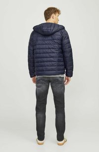 Chaqueta de plumas navy con costuras horizontales, capucha y puños elásticos, combinada con jeans oscuros y zapatos de color claro.