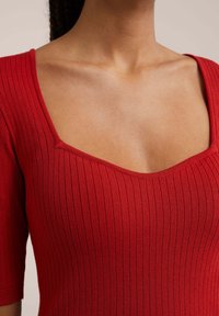 Rotes geripptes Strickoberteil mit quadratischem Ausschnitt und kurzen Ärmeln, das eine figurbetonte Passform und eine glatte Textur aufweist.