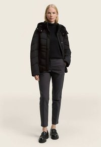 Crna puhasto jakna s uklonjivim kapuljačom, zatvaranjem na patentni zatvarač i kopčama na drukere, nošena sa uskim tamnim hlačama i crnim mokasinkama.