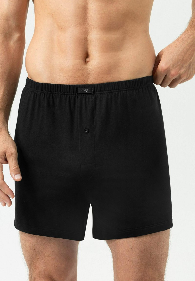 Boxers en coton noir avec une ceinture élastique douce, dotés d’un bouton à l’avant et d’une texture lisse, présentés sur un torse masculin.