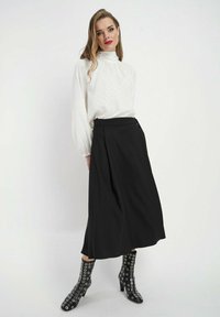 Biała bluzka z długim rękawem w kropki, czarna spódnica midi oraz czarne botki za kostkę z ozdobnymi srebrnymi oczkami. Prosta i elegancka sylwetka.