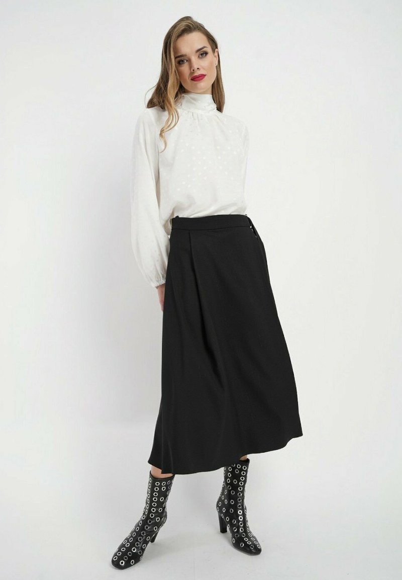 Biała bluzka z długim rękawem w kropki, czarna spódnica midi oraz czarne botki za kostkę z ozdobnymi srebrnymi oczkami. Prosta i elegancka sylwetka.