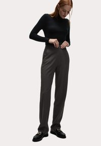 Op maat gemaakte antracietgrijze broeken met een hoge taille, textuurstof en zijzakken, gecombineerd met een aansluitende zwarte coltrui en loafers.