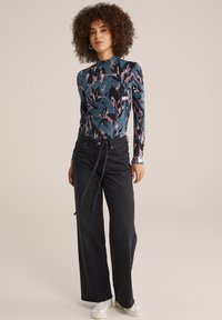 Haut à manches longues, ajusté, de couleur bleue avec des motifs roses et noirs, associé à un jean noir à taille haute et jambes larges, et des baskets blanches.