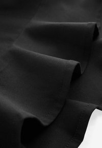 Gros plan sur un tissu noir avec une texture de tissage visible et une couture d'ourlet incurvée sur les bords pliés.