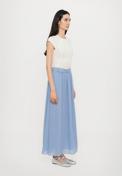 Biela blúzka s krátkymi rukávmi so švami, skombinovaná s bledomodrou plisovanou maxi sukňou so širokým pásom. Outfit dopĺňajú strieborné ploché topánky.