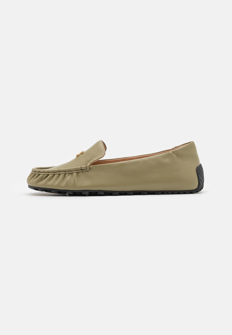 Mocassin en cuir marron clair à enfiler avec semelle en caoutchouc noire et détails de coutures subtils sur un fond blanc uni.
