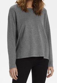 Grå långärmad tröja i ett mjukt stickat tyg med en avslappnad passform, med rundad halsringning och sidoventiler, kombinerad med mörka byxor.