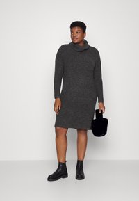 Vestido cinza com gola alta, feito de tecido texturizado, mangas longas, design até ao joelho, combinado com botas pretas de tornozelo e uma bolsa preta.