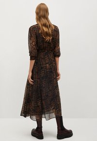 Braun gemustertes langes Kleid mit gebundenem Taillenzug, semi-transparenter Stoff, Ballonärmeln und getragen mit klobigen schwarzen Stiefeln.