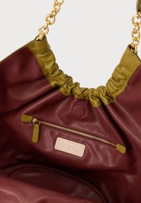 Borsa tote in pelle color marsala e verde oliva con manico a catena, apertura arricciata, tasca interna con zip, ferrature dorate e etichetta con logo in rilievo.