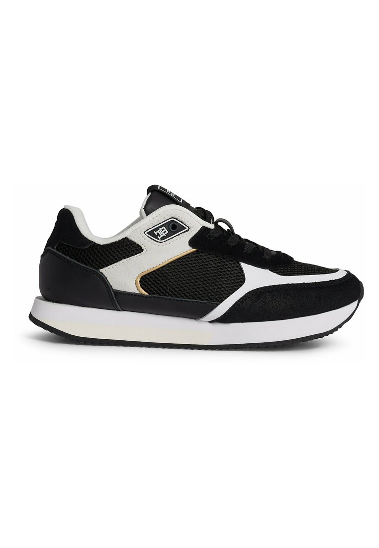 Zapatillas deportivas en blanco y negro con parte superior de malla, acentos de ante, cuello acolchado y suela de goma texturizada. Presentan cordones negros y un logo.
