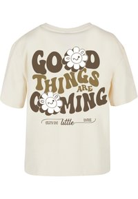 T-shirt color crema con una grafica che riporta il testo "Buone cose stanno arrivando" in marrone, accompagnato da disegni di fiori sorridenti e pecore.