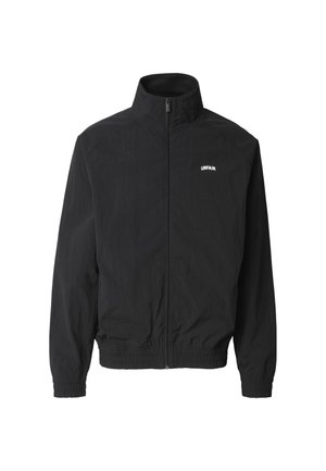 Czarna kurtka na zamek z wysokim kołnierzem, elastycznymi mankietami i pasem, z małym białym napisem "UNFAIR" na lewej piersi.