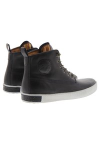 Zapatillas altas de cuero negro con un logo redondo, seis ojales y una suela de goma blanca con un acento texturizado a lo largo del talón.