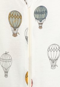 Tissu blanc avec des illustrations colorées de montgolfières en bleu, orange et gris. Fermeture éclair au centre.