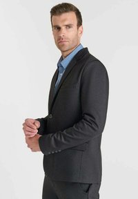 Blazer grigio scuro realizzato in tessuto texturizzato, con un solo bottone, rever a punta e due tasche frontali. Indossato su una camicia azzurra chiara.