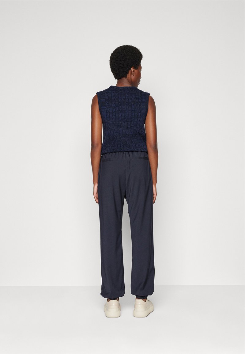 Granatowy dzianinowy top bez rękawów z teksturowanym wzorem, w połączeniu z luźnymi ciemnymi spodniami i jasnymi sneakersami. Minimalistyczny design.