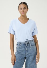 Světle modré tričko s výstřihem do V z jemné látky, krátké rukávy, spárované s vysokými modrými džíny z denimu s detaily na zavazování v pase.
