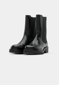 Black ankle boots made of glossy material, featuring elastic side panels, a chunky sole, and a rounded toe design.