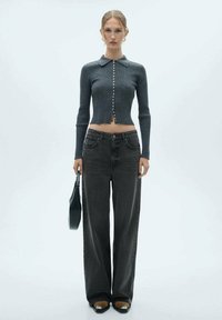 Sivi pleteni crop top s detaljima od dugmadi i ovratnikom, uparen s širokim crnim trapericama i malom crnom torbicom. Glatka tekstura, ležeran stil.