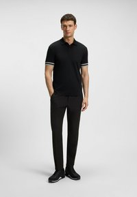 Svart polo skjorta med randiga ärmslut, i kombination med svarta byxor och sneakers. Slätt tyg och skräddarsydd passform, med en klassisk krage.