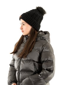 Chaqueta de plumas negra con capucha, con una textura acolchada y un acabado brillante, combinada con un gorro negro de canalé rematado con un pompón.