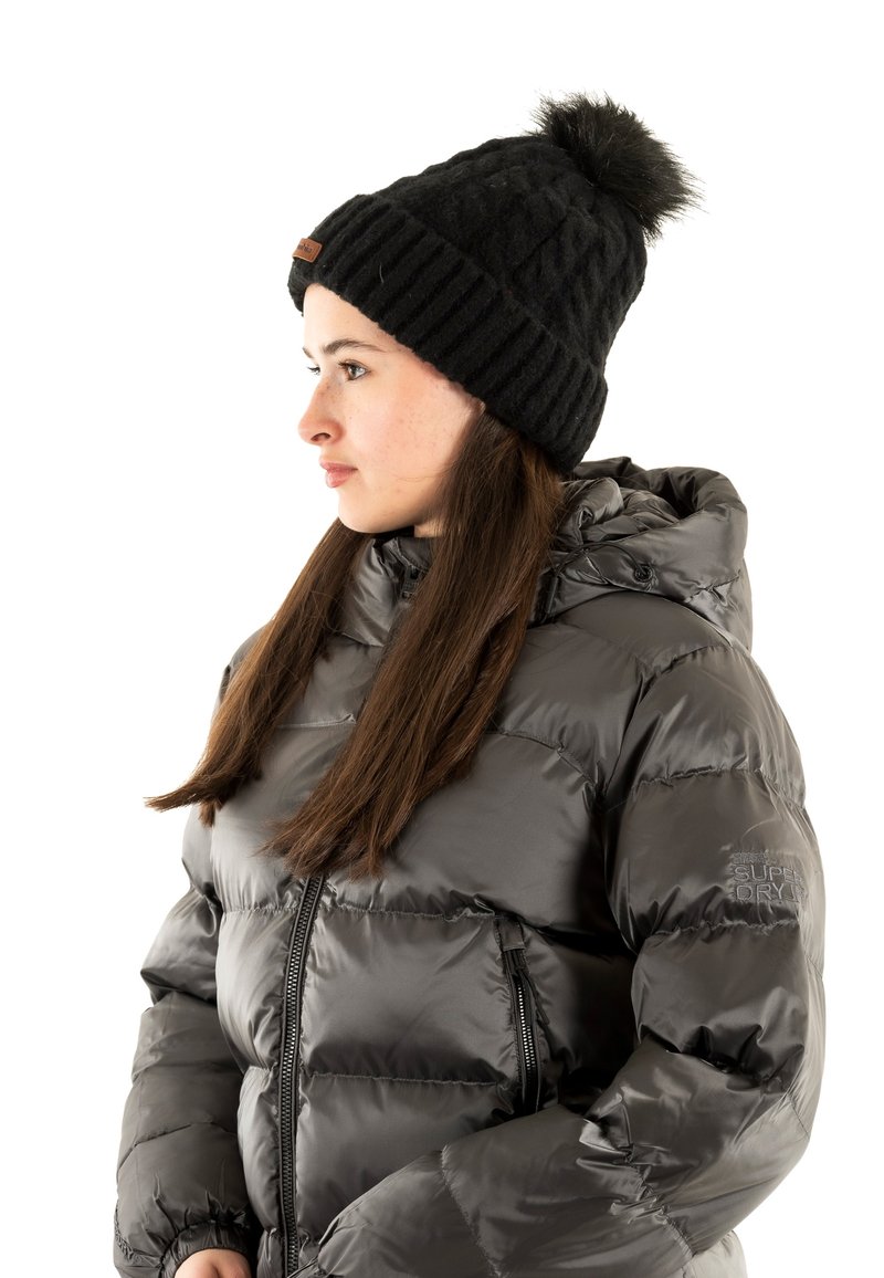 Chaqueta de plumas negra con capucha, con una textura acolchada y un acabado brillante, combinada con un gorro negro de canalé rematado con un pompón.