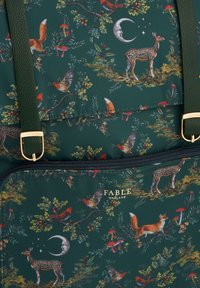 Zelena ruksak s uzorkom šume s jelenima, lisicama, pticama i gljivama. Zlati detalji naglašavaju zatvaranje na zip i naramenice.