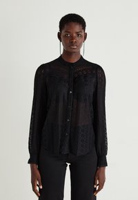 Schwarze Spitzenbluse mit langen Ärmeln, floralem Muster und transparenten Abschnitten, mit durchgehender Knopfleiste und rundem Kragen. Details umfassen strukturierte Akzente.