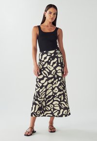Czarna i kremowa długa spódnica w abstrakcyjne wzory, zestawiona z dopasowanym czarnym topem na ramiączkach i eleganckimi czarnymi sandałami.