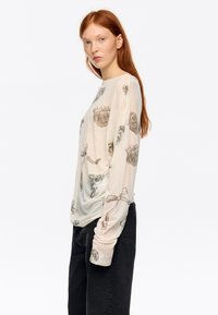 Bluzka z długim rękawem, lekka, w kolorze kremowym z kwiatowym wzorem w stonowanych tonacjach. Charakteryzuje się luźnym krojem, miękką fakturą i okrągłym dekoltem.