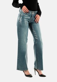 Jeans de mezclilla azul claro con diseño de pierna ancha, acabado brillante, bolsillos frontales clásicos y cintura alta. Tacones altos negros visibles.