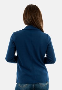 Blazer texturizado azul marino con solapa, silueta ajustada y mangas largas; combinado con jeans de denim claros.